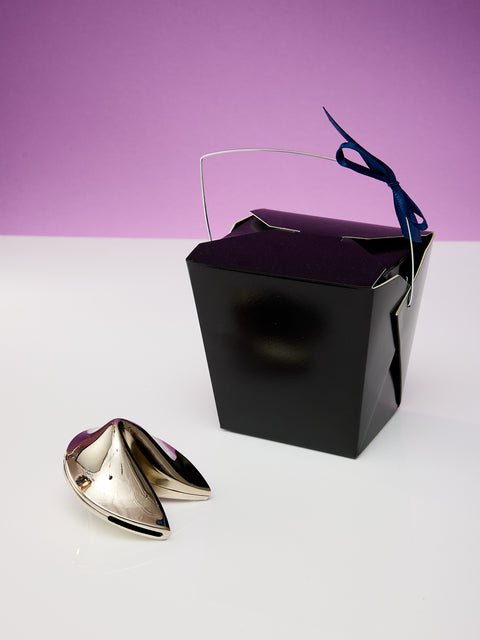 Chrome fortune cookie next to a black take out box.