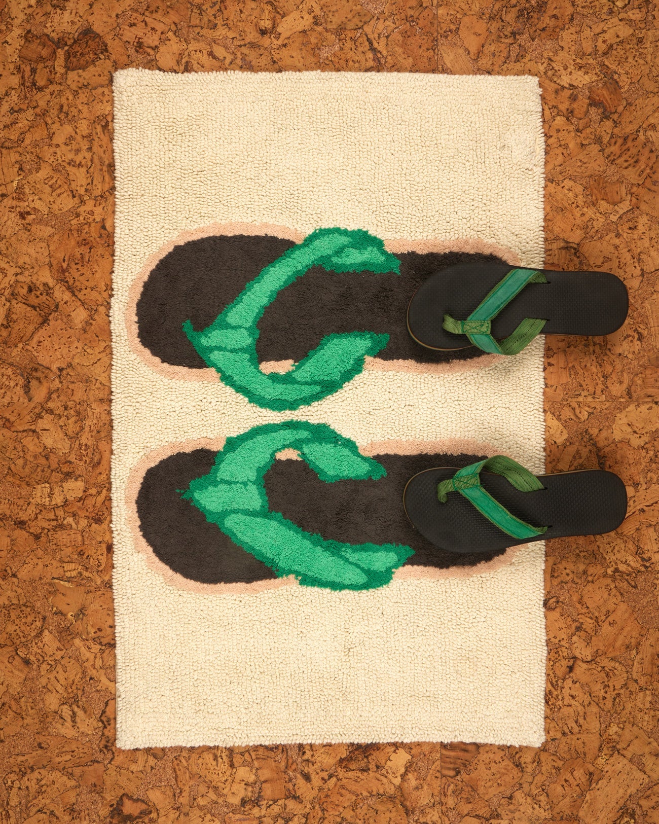 A pairs of black and green flip-flops on a textured bath mat with flip flop design on a cork-like background.