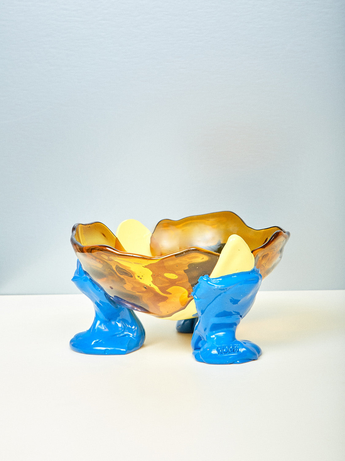 A sculptural resin bowl with blue legs and an amber bowl, handmade in Italy.