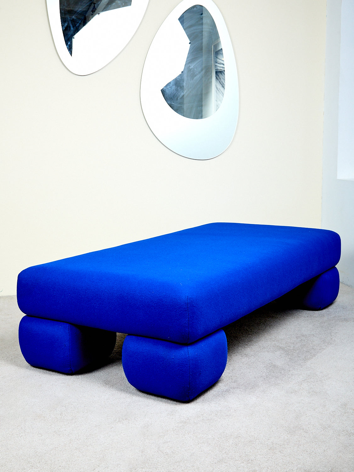 A blue daybed with chunky pedestal feet against a white background.