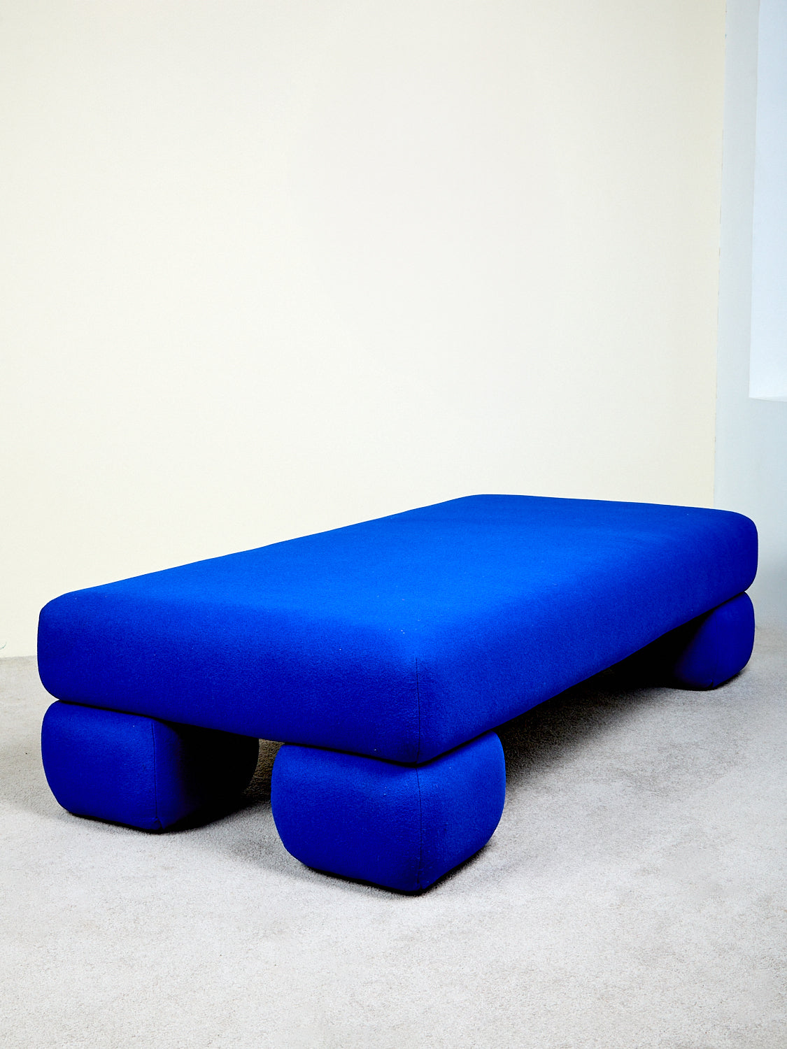 A blue daybed with chunky pedestal feet against a white background.