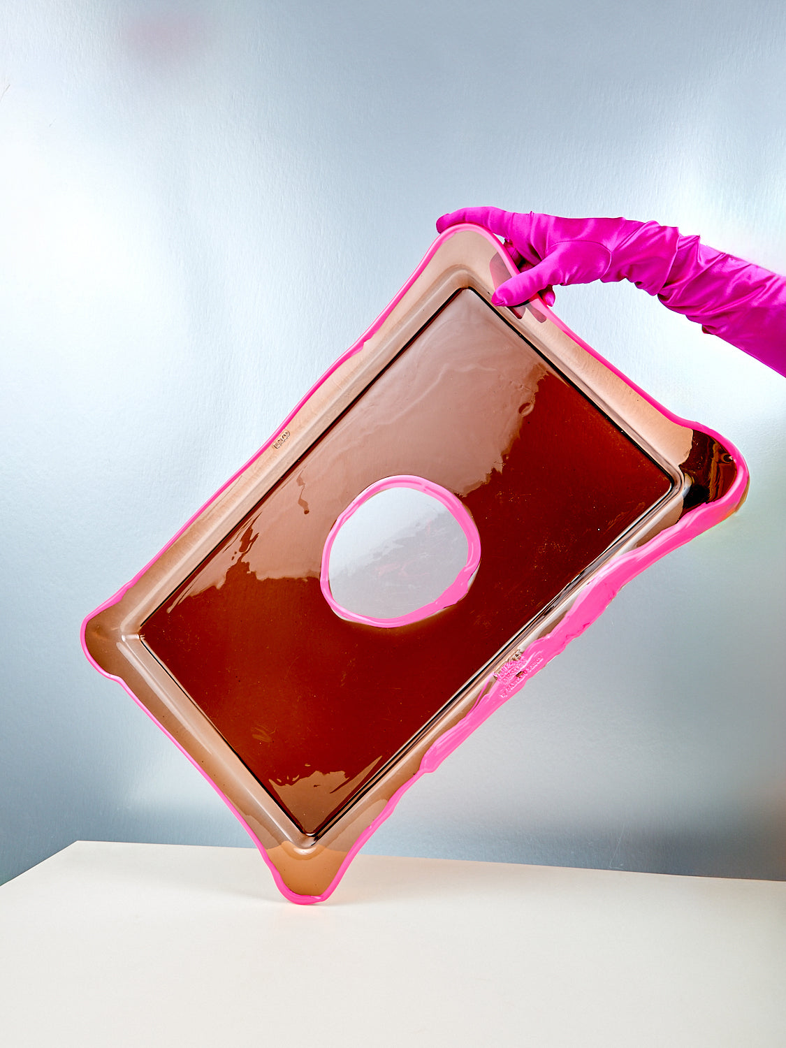 Pink and brown rectangular object with a circular cutout, held by a gloved hand against a gray background.