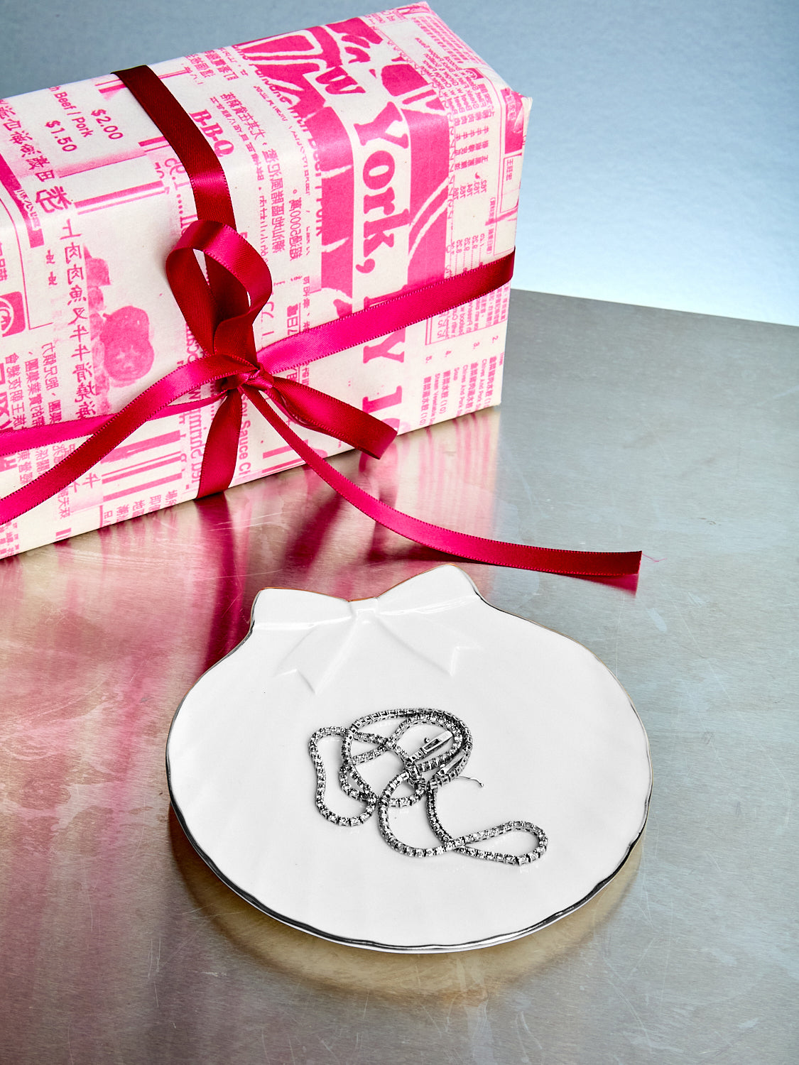 Silver necklace on a white dish with a wrapped gift in the background