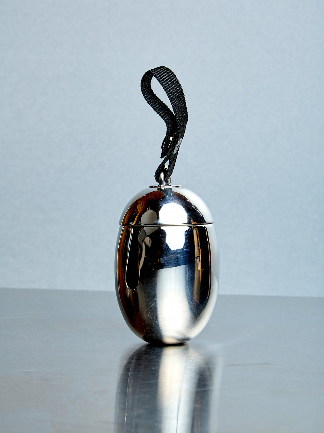 Silver metallic object with a black strap on a reflective surface and light gray background