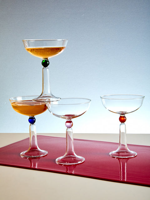Set of four cocktail glasses with colored stems on a red surface