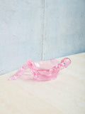 Pink glass bathing lady dish on a textured surface with a light blue background
