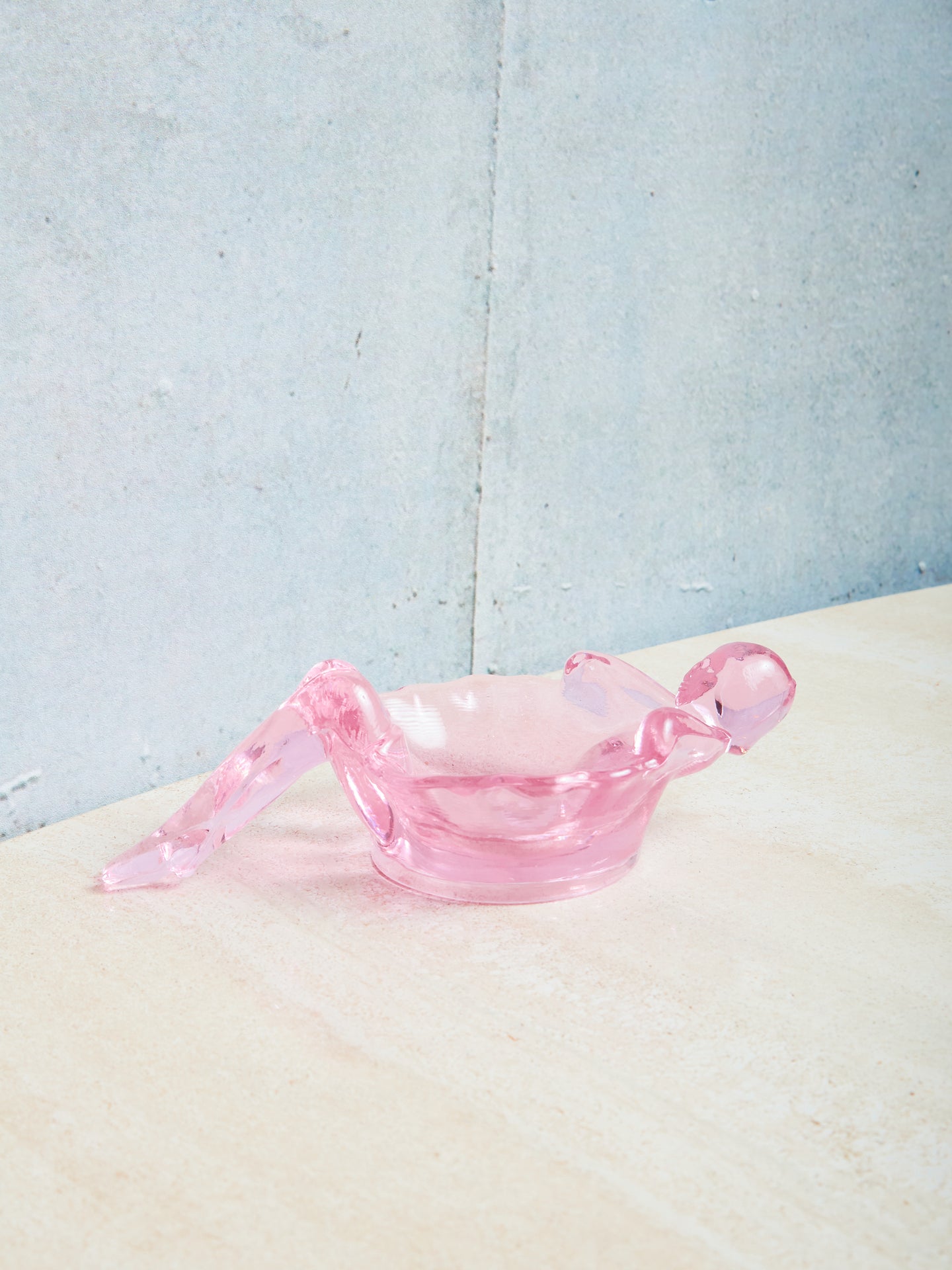 Pink glass bathing lady dish on a textured surface with a light blue background