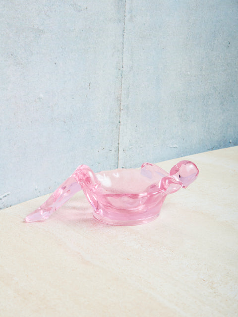 Pink glass bathing lady dish on a textured surface with a light blue background