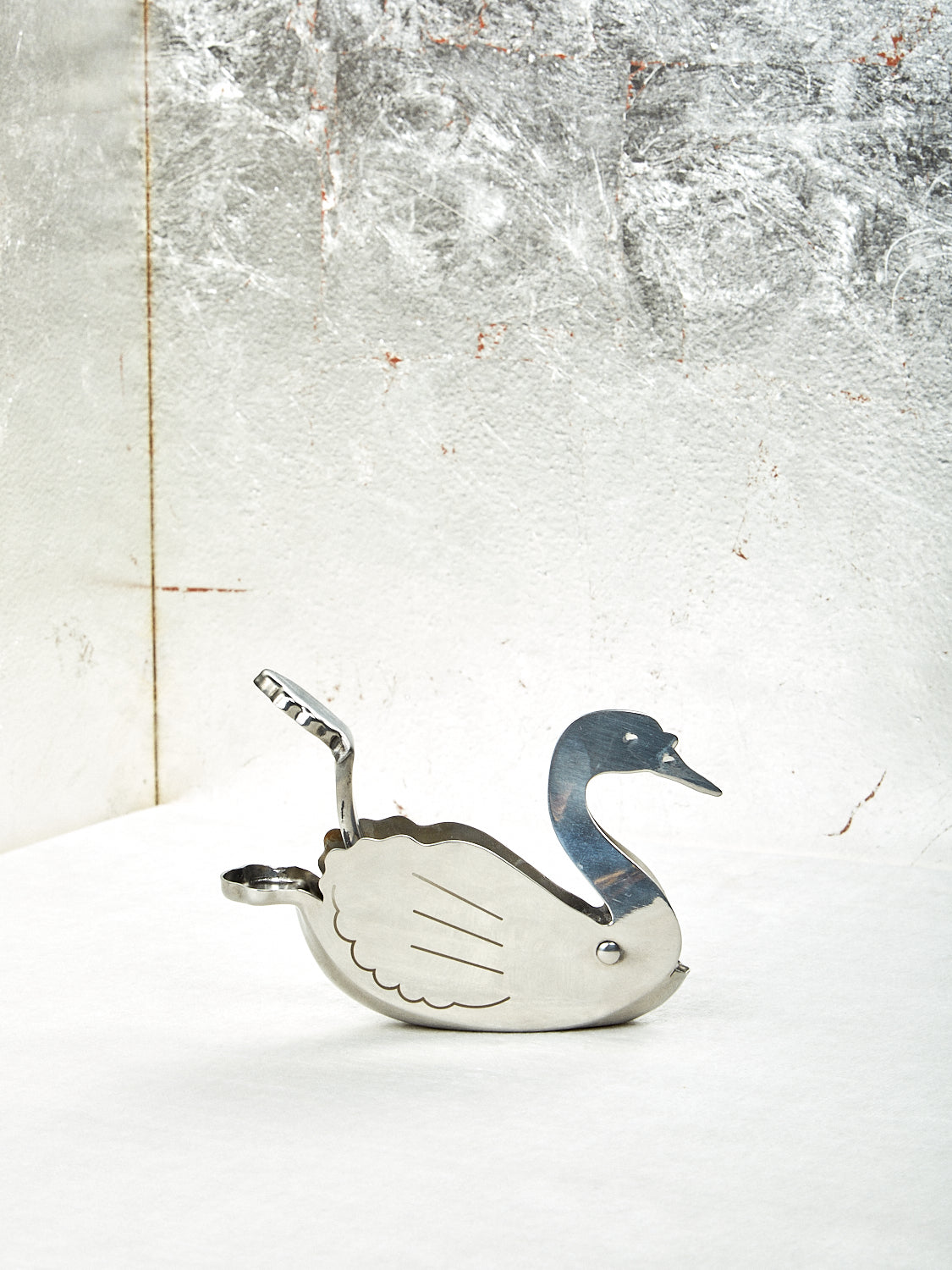 A silver Swan lemon squeezer with a decorative bird design on a textured background.