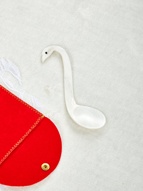 A hand-carved mother of pearl spoon designed in the shape of a swan, displayed on a red and white surface.