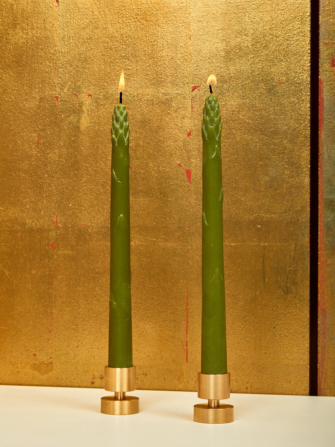 A pair of lit asparagus shaped dinner candles in small brass holders.
