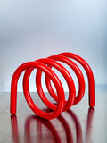 Red metal spiral stand on a reflective surface with a light gray background