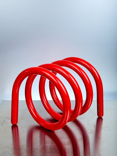 Red metal spiral stand on a reflective surface with a light gray background