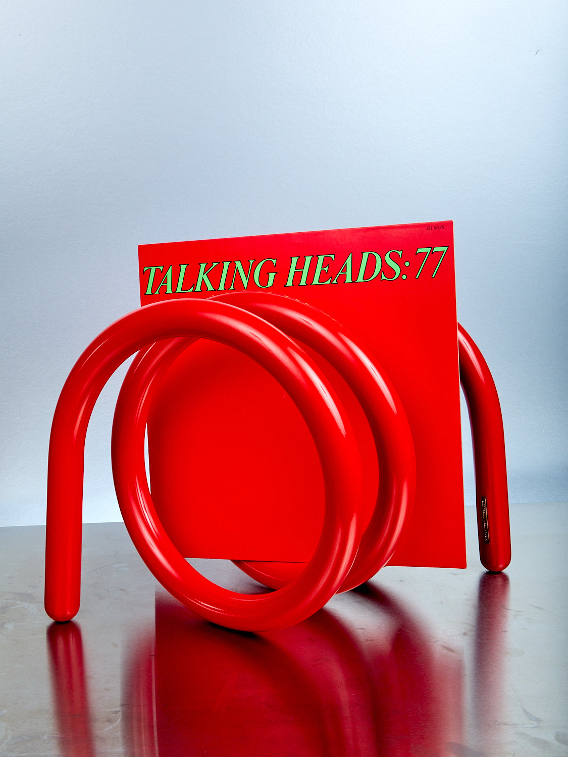 Red spiral stand with with 'TALKING HEADS:77' record on a reflective surface