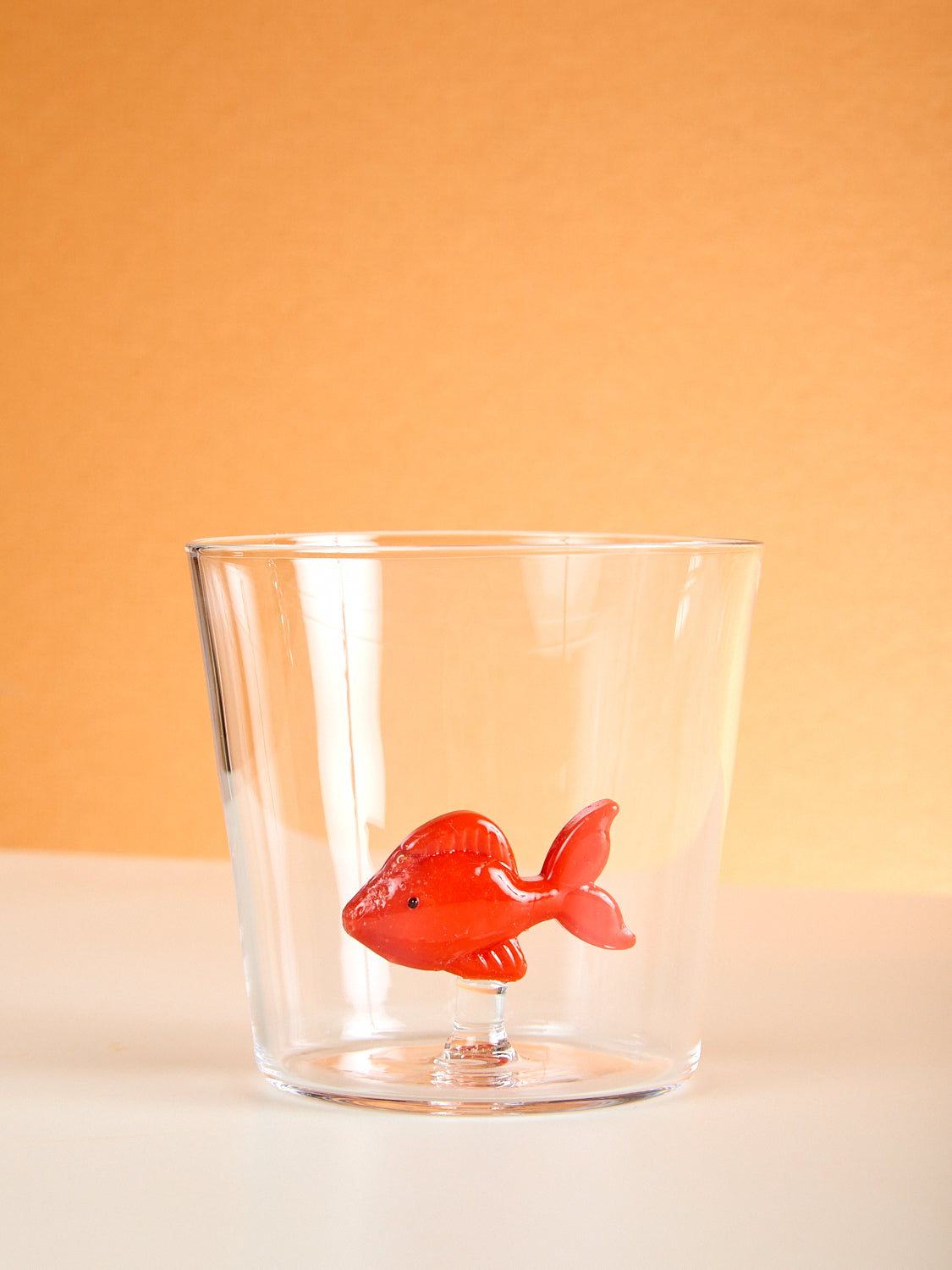 A small cup with a red fish made of glass inside it.