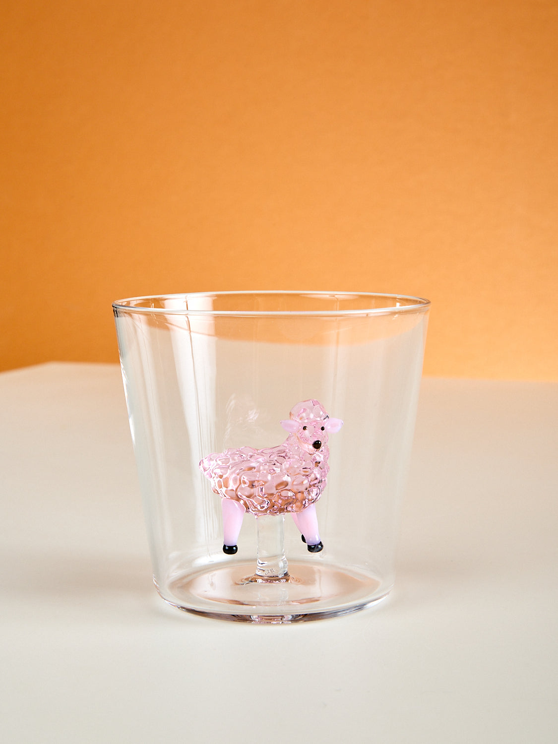 A small cup with a pink sheep made of glass inside it.