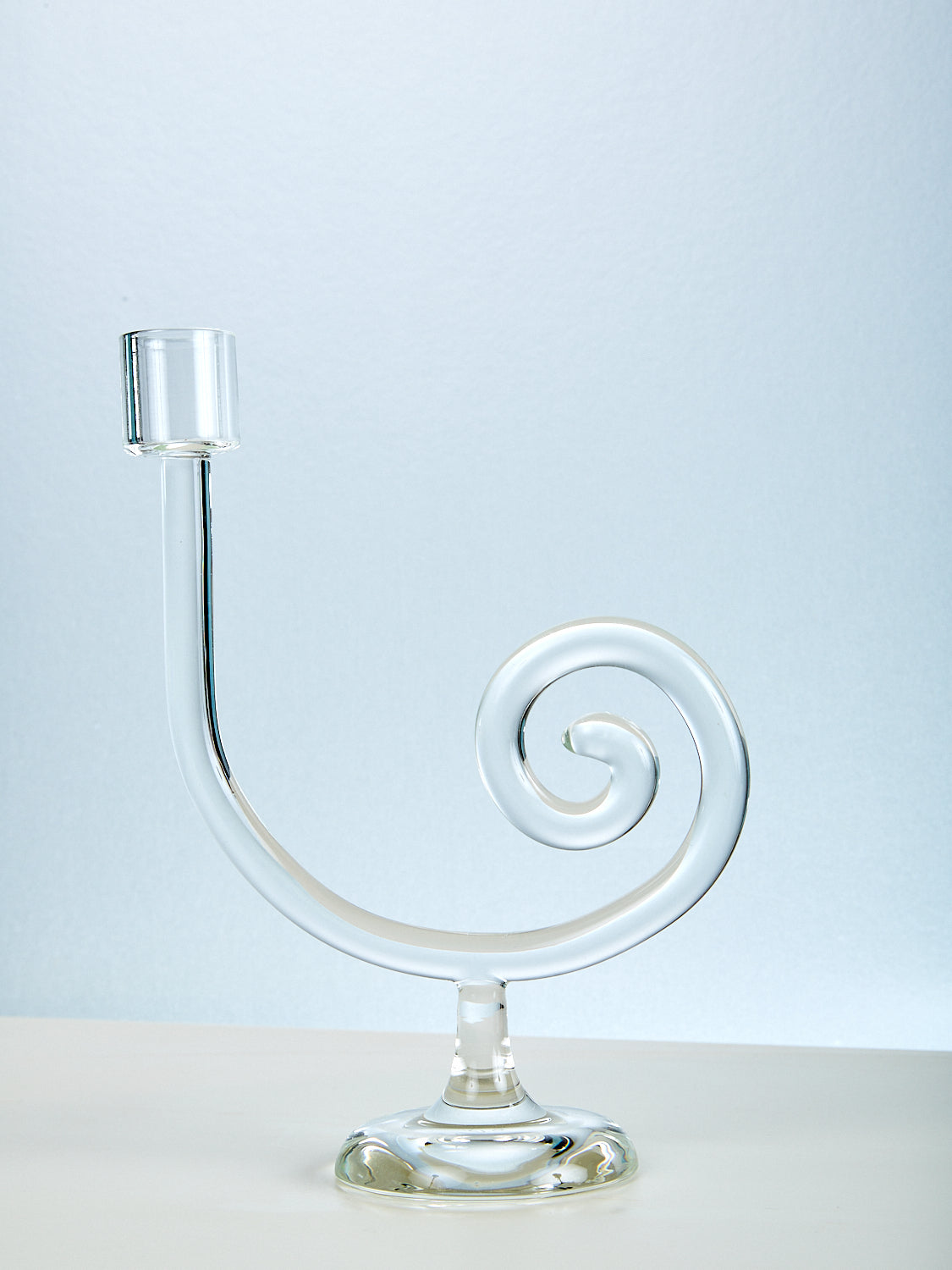 Clear glass candle holder with spiral design on a light blue background