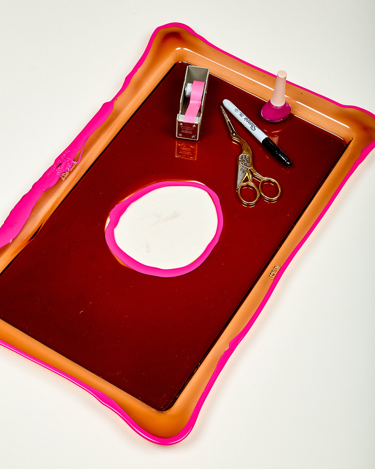 Red tray with pink border containing stationery items on a white background