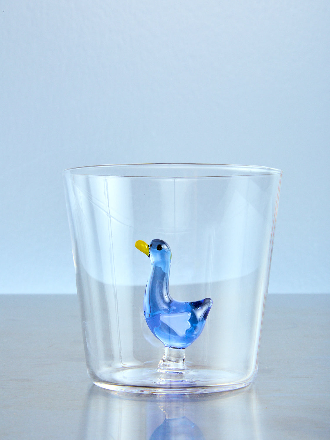 Clear glass tumbler with a blue goose figurine on a light blue background