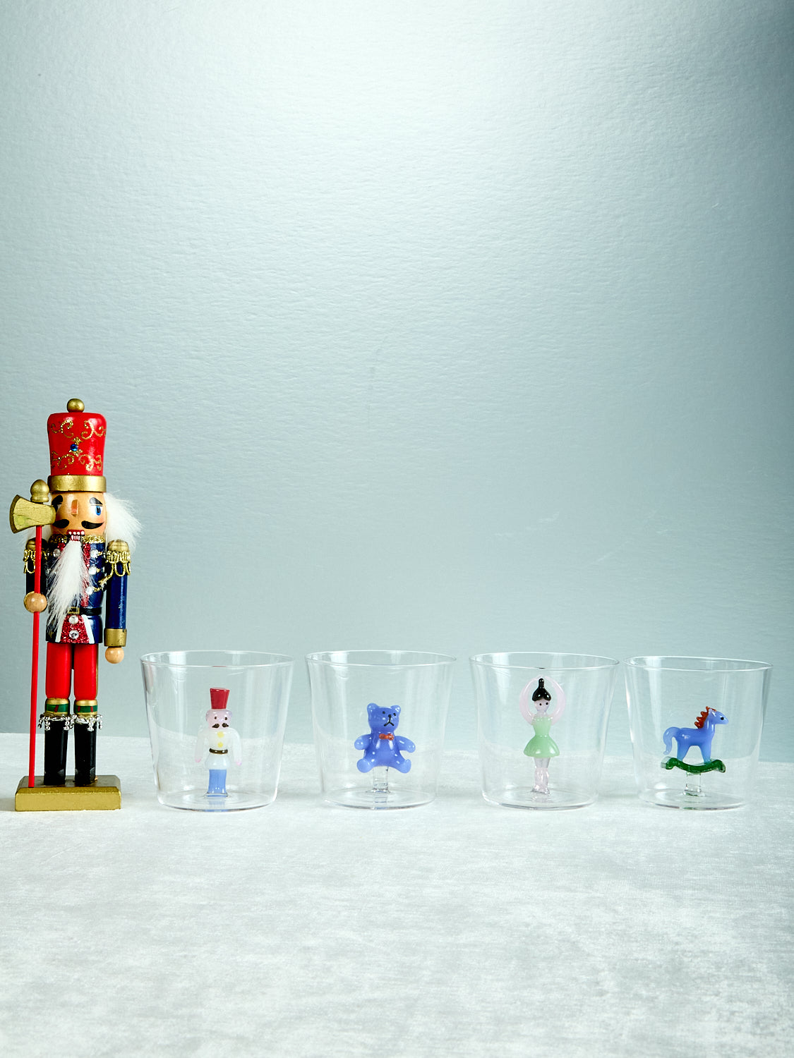 Set of four glass tumblers with miniature figurines on a light gray background, accompanied by a nutcracker figurine.