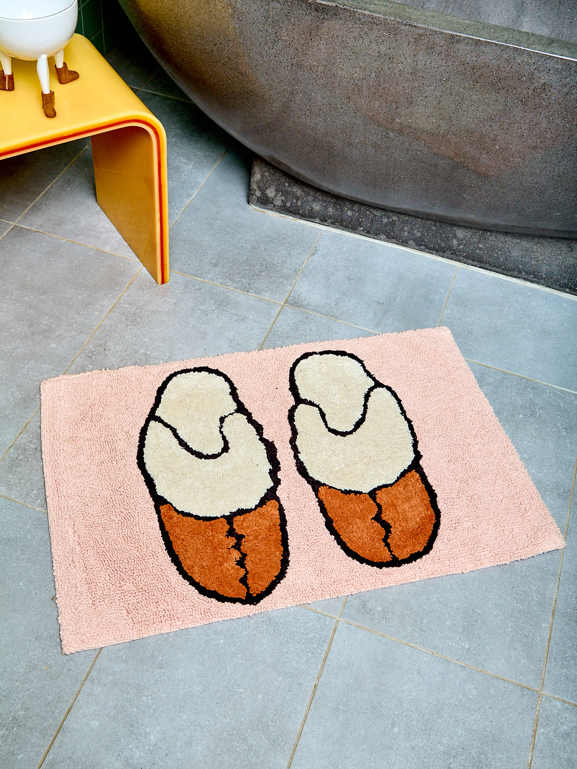 Bath mat with suede slipper design on a tiled floor