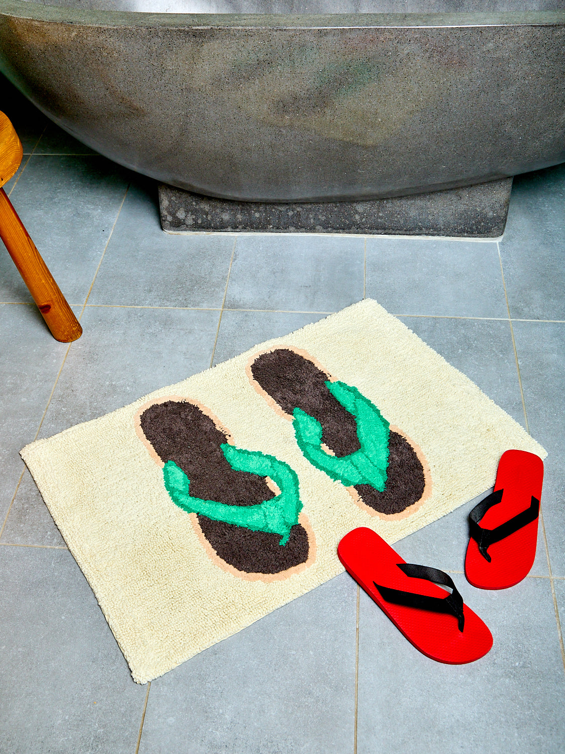 Bath mat with flip-flop designs on a tiled floor next to a bathtub.