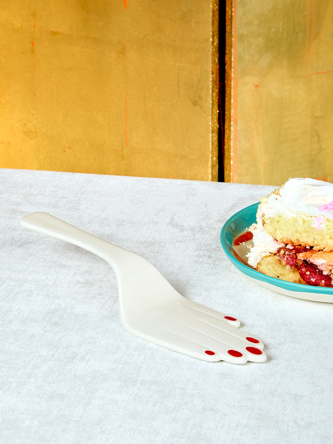 White hand shaped cake server on a white surface, next to a plate of cake.