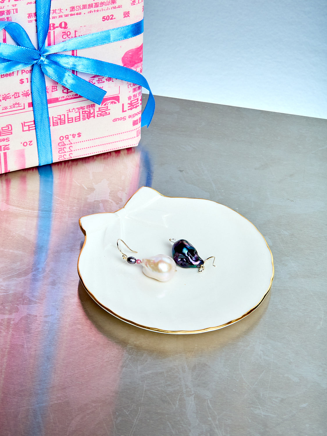 Jewelry dish with earrings on a reflective surface next to a wrapped gift.