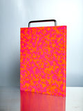 Pink and orange patterned chopping block on a metal surface with a light gray background