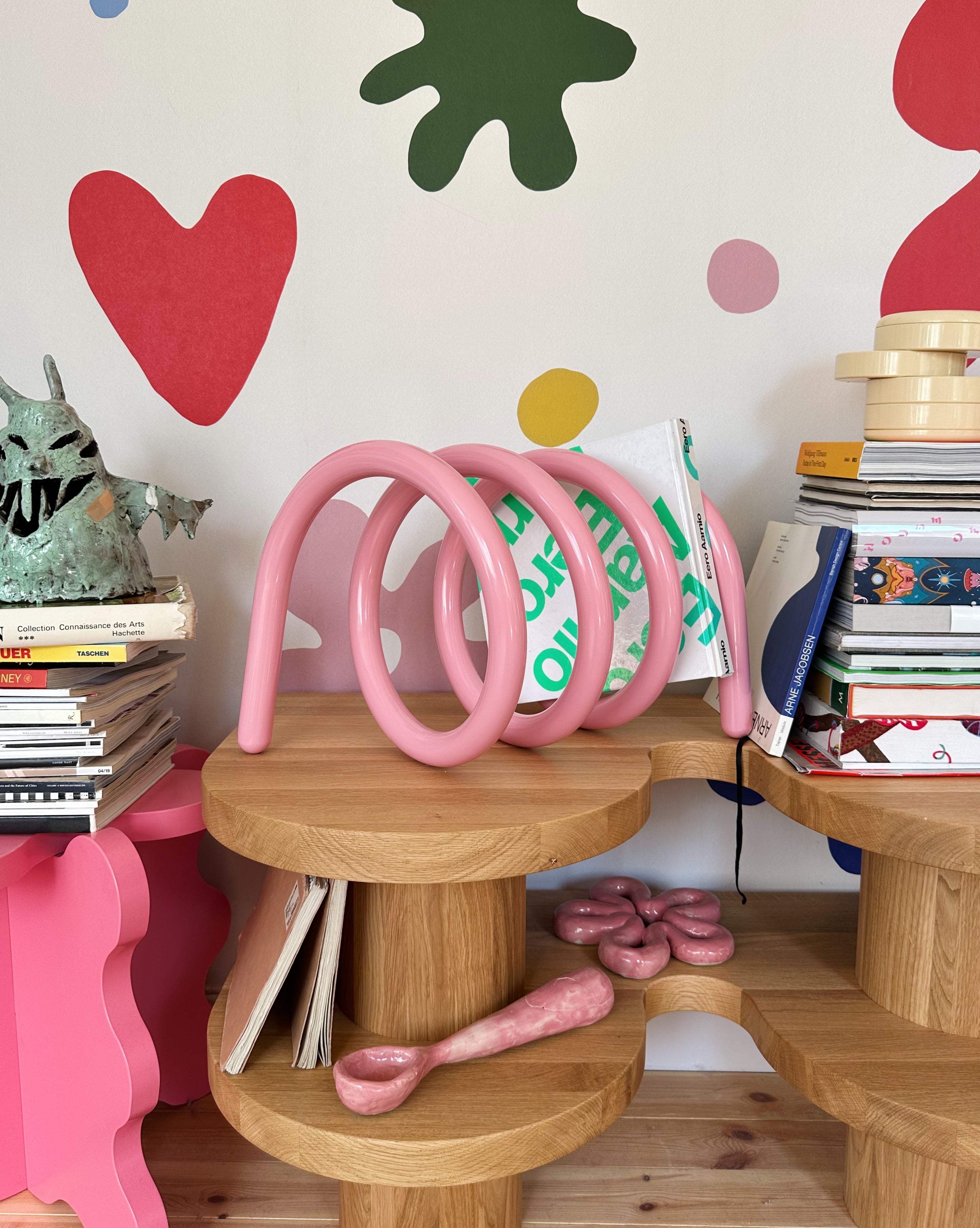 Wooden shelf with pink spiral stand against a colorful wall with hearts and circles.